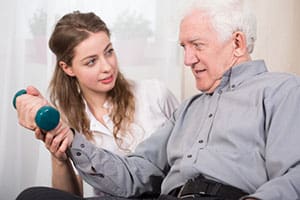 In home care professional assisting elderly man with physical therapy