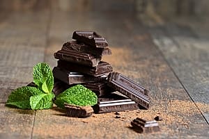 Dark chocolate pieces stacked on wooden table with mint leaf